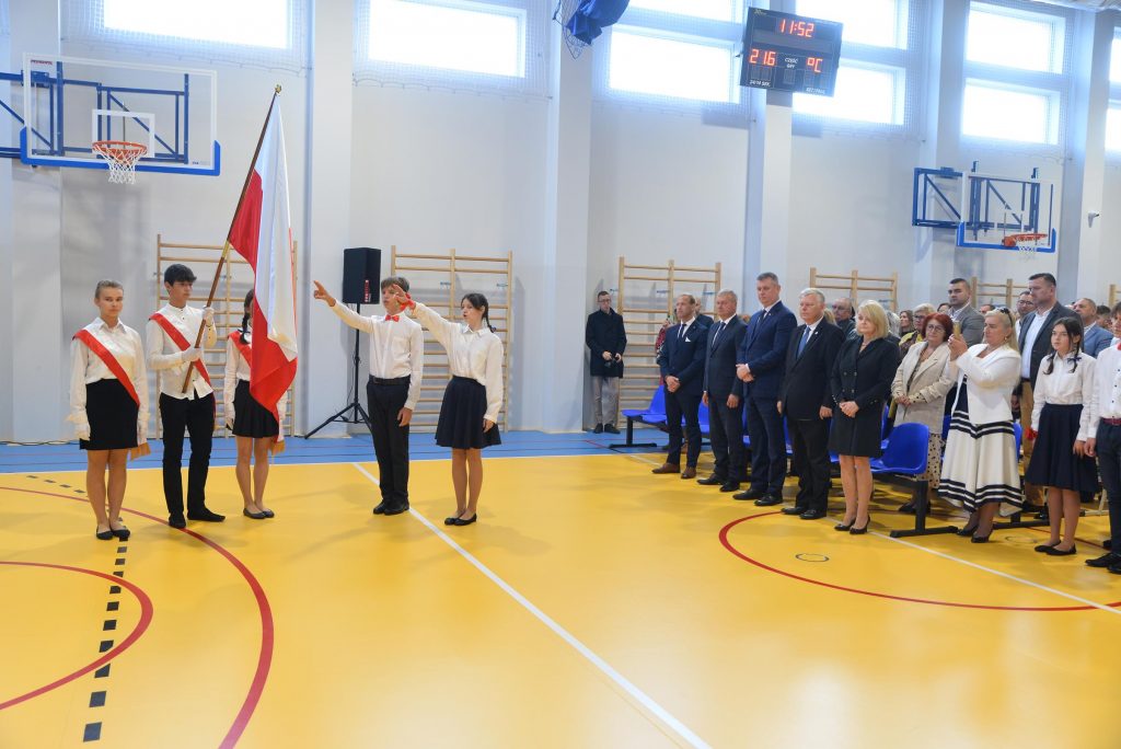 zdjęcie przedstawia wnętrze sali gimnastycznej w PSP Cerekiew. Po prawi stronie są zaproszeni goście a na wprost poczet sztandarowy z flagą Polski