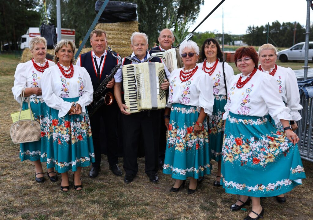 Kapela ludowa w barwnych strojach-kobiety a po środku trzej mężczyźni z instrumentami.