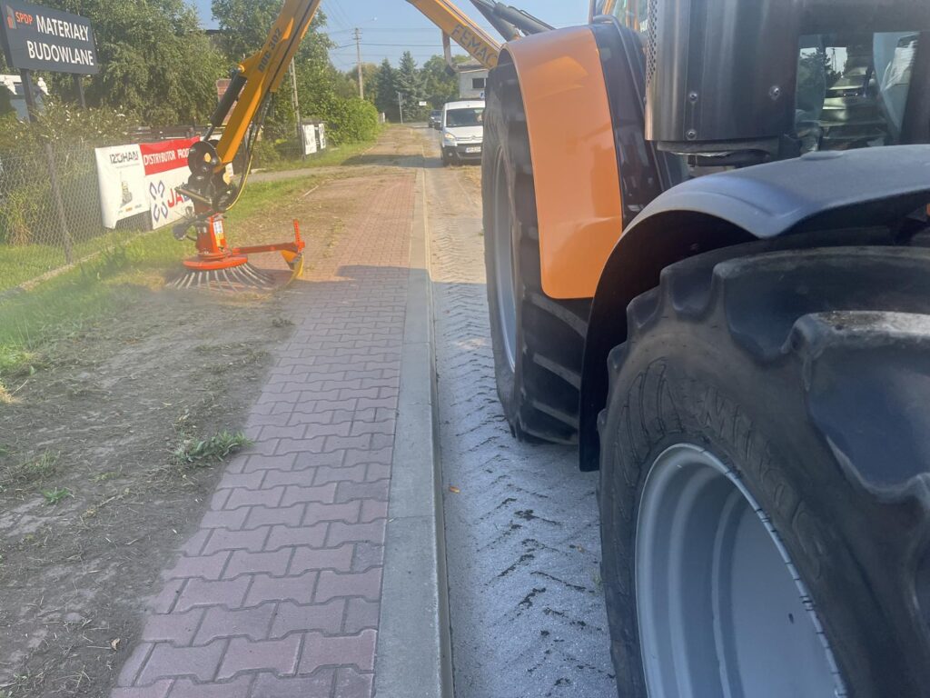 Odchwaszczanie chodnika z wykorzystanie nowego urządzenia, w tle zabudowania.