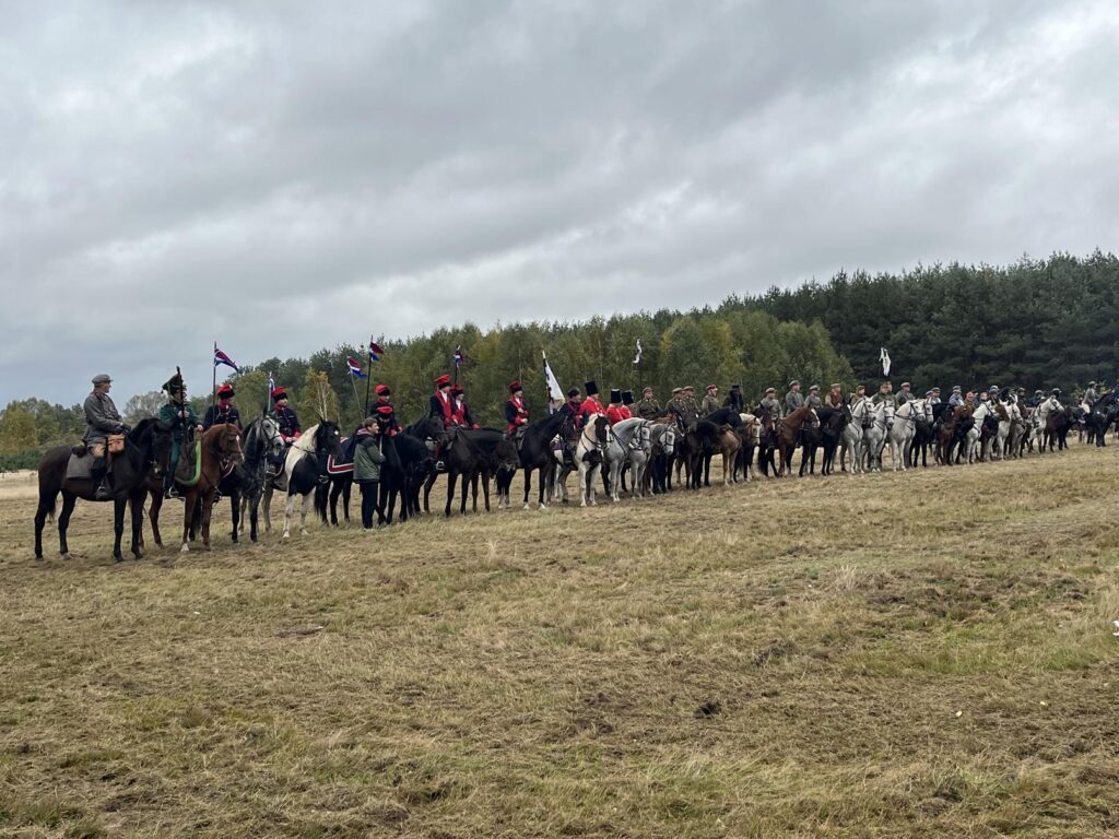 Duża grupa jeźdźców na koniach  przygotowujących się XIII Hubertusa. W tle drzewa.