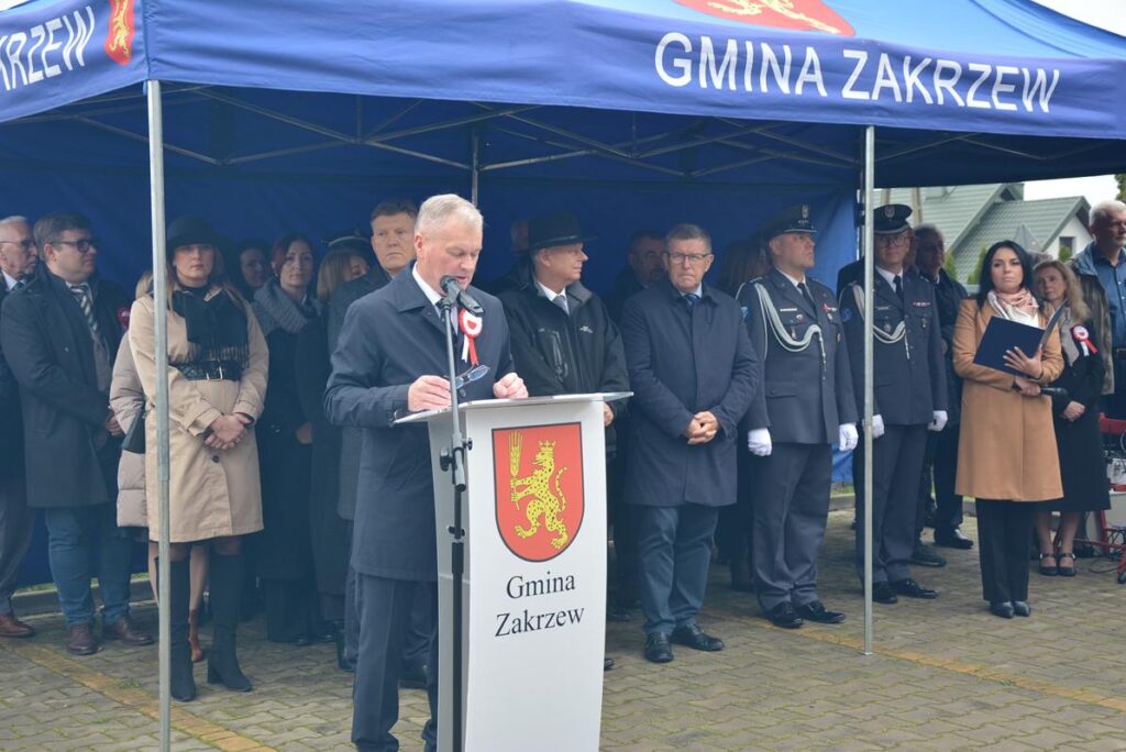 Przemówienie Wójta Gminy Zakrzew - przy mównicy z napisem Gmina Zakrzew. W tle grupa osób.