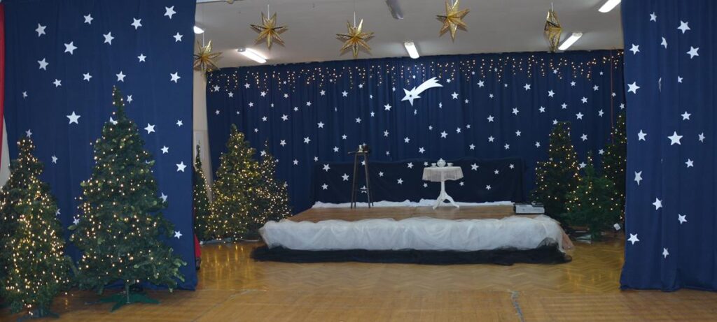 Na zdjęciu przedstawiona jest inscenizacja jasełek, czyli przedstawienia bożonarodzeniowego, przygotowanego przez dzieci i młodzież. Scena udekorowana jest w świątecznym klimacie: w tle widać granatową kurtynę z gwiazdami, świecące lampki oraz choinki, co tworzy nocną, betlejemską scenerię.