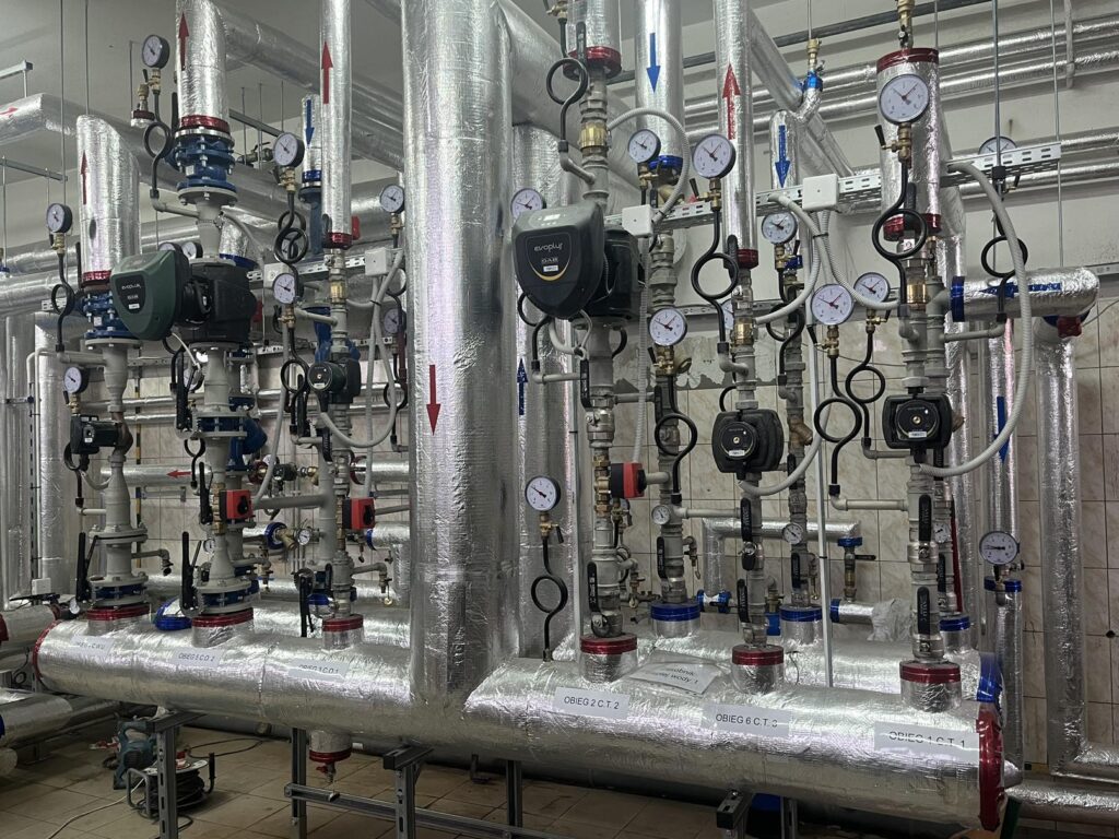 Instalacja grzewcza z izolowanymi rurami, zaworami, manometrami i pompami obiegowymi, tworząca rozdzielacz systemu ogrzewania w kotłowni